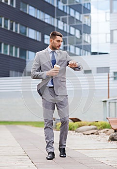 Young serious businessman with paper cup outdoors