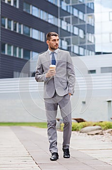 Young serious businessman with paper cup outdoors