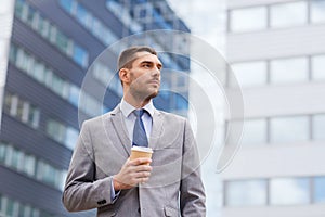 Young serious businessman with paper cup outdoors