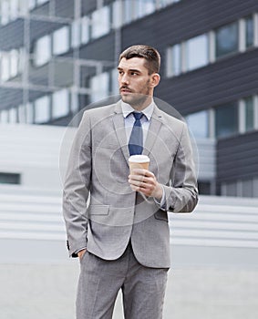 Young serious businessman with paper cup outdoors