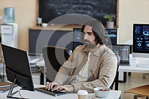 Young serious businessman typing on keyboard and looking at computer screen
