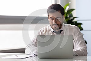 Young serious businessman working at laptop in office.