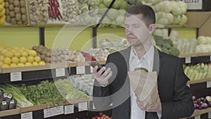 Young serious Caucasian man hanging up the phone in grocery and sighing. Confident businessman in touch as making