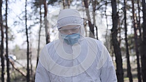 Young serious caucasian man in safety suit walking in city park. Handsome boy wearing protective gloves and face mask