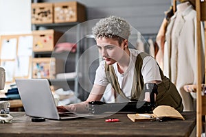 Young serious fashion designer looking at new trendy attire on laptop screen