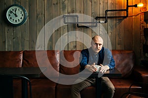 Young serious fashionable man sitting alone in loft-styled cafe