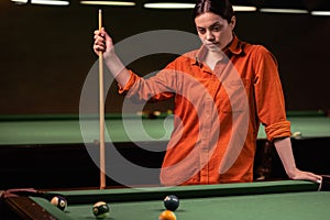 Young serious girl playing billiards in the club stands thinking near the table, billiard sport