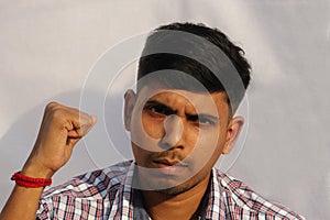 Young serious looking Indian man close up face portrait with fist up view on isolated dark background.
