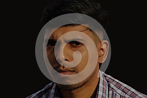 Young serious looking Indian man close up face portrait view on isolated dark background.