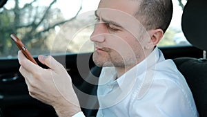 Young serious man with a beard sitting in the car and holds the phone