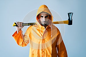 Young serious man in bright raincoat holding big ax on his shoulder