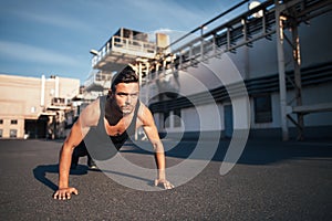 Young serious man doing pushups outdoor on industrial background