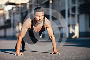 Young serious man doing pushups outdoor on industrial background