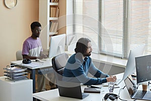Young serious man pressing keys of computer keyboard by workplace