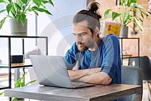 Young serious man working, studying using laptop sitting in coworking cafe