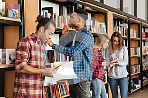 Young serious men students standing in library reading books