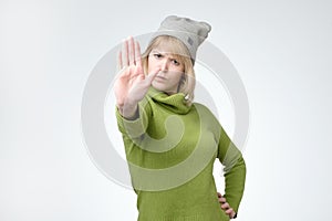 Young serious pretty girl in green sweater and hat showing stop sign