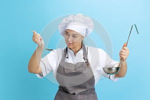 Young serious woman, lady-cook, chef in white uniform cooking isolated on blue background. Cuisine, profession, business