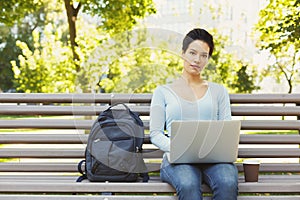 Young serious woman using laptop in park, copy space