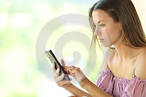 Young serious woman using smart phone near a window