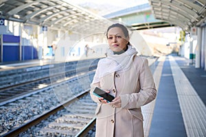 Young serious woman waiting train on platform of railway station.