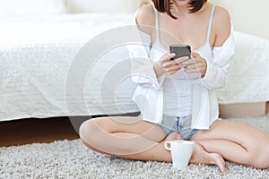 Young sexy asian woman wearing white dress and short hairs using cell phone while drinking coffee in bedroom relaxation with