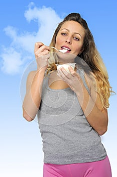Young and attractive blond girl with spoon eating natural cream yogurt in diet healthy nutrition
