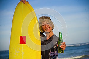 Young beautiful and happy surfer woman holding yellow surf board smiling cheerful drinking beer bottle enjoying summer holida