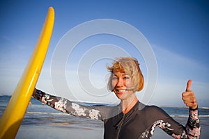 Young beautiful and happy surfer woman holding yellow surf board smiling cheerful enjoying summer holidays in tropical beach