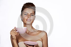 Young beautiful woman with dark hair picked up holding a ceramic cup and saucer pale pink drink tea or coffee on a white back