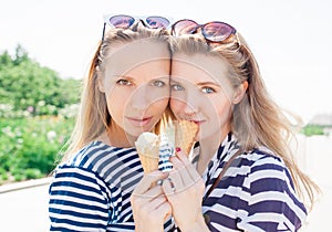 Young blonde best friends girls eating ice cream in summer hot weather in sunglasses have fun and good mood looking in camera