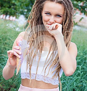 Young blonde girl with dreads eating multicolored ice cream in waffle cones in summer evening, joyful and cheerful. Europea