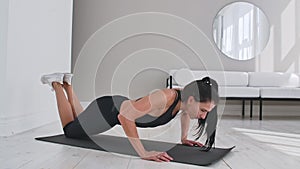 Young sexy brunette woman in sportswear performs pushups kneeling at home on a rug.