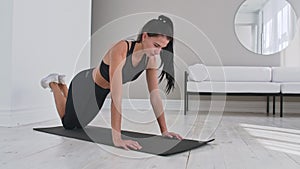 Young sexy brunette woman in sportswear performs pushups kneeling at home on a rug.