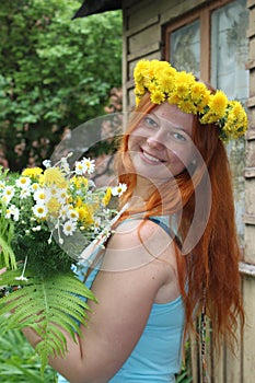 Young sexy caucasian girl with red hair laughs merrily. The girl has a wreath of dandelions on her head and a large bouquet of