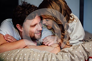 Young couple in love lying in bed in hotel, embracing on white sheets, close up