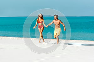 Young sexy couple running on sandy beach near ocean