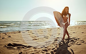 Young sexy female surfer is holding a surfboard and walking the beach at sea. Summer, vacation, sea