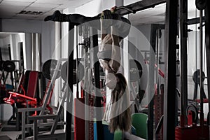 Young fitness girl pulls up in the gym and performing exercises on the horizontal bar