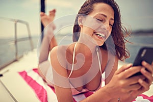 A young sexy girl is happy because of a message she got on a smartphone while is enjoying a sunbath. Summer, sea, vacation