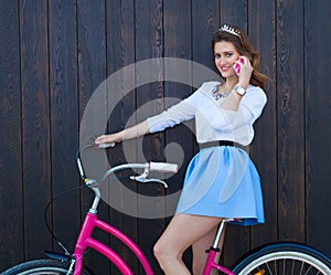 Young girl with long hair with pink phone standing near vintage pink bicycle and speaking on the phone, have fun and good moo