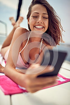 A young sexy girl is reading a message on a smartphone while enjoying a sunbath. Summer, sea, vacation