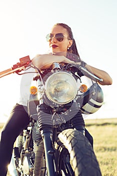 Young girl sitting on vintage custom motorcycle and drinking juice . Outdoor lifestyle portrait