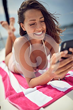 A young sexy girl is using a smartphone while is taking a sunbath. Summer, sea, vacation