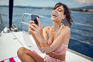 A young sexy girl who is sitting on the towel and having a good time while chatting on a smartphone and enjoying a sunbath on a