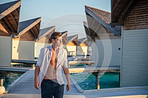 Young sexy handsome man wearing shirt walking near over water villas at the tropical island luxury resort