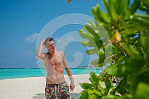 Young sexy man in swimming shorts standing at the beach at the tropical island