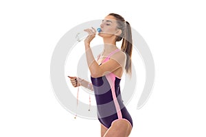 Young sports woman in body swimsuit with measure tape in hand drinks water isolated on white background