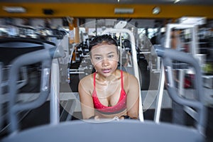 and sweaty Asian woman training hard at gym using elliptical pedaling machine gear in intense workout photo