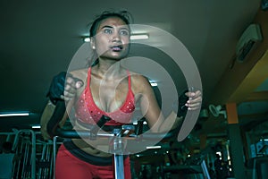 Young and sweaty Asian woman training hard at gym using elliptical pedaling machine gear in intense workout exercise photo